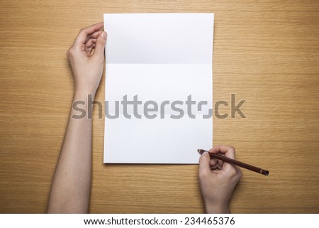 A female(woman) hands hold a empty(blank) white letter with a pencil on the desk(table), top view at the studio.
