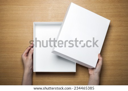 A female(woman) hands hold a empty(blank) white box on the desk(table) top view at the studio.