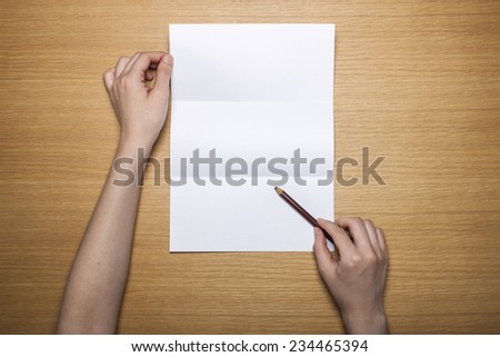 A female(woman) hands hold a empty(blank) white letter with a pencil on the desk(table), top view at the studio.