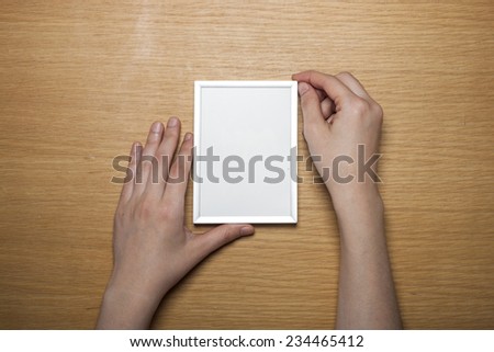 A female(woman) hands hold a steel photo(picture) empty(blank) frame on the desk(table)  top view at the studio.