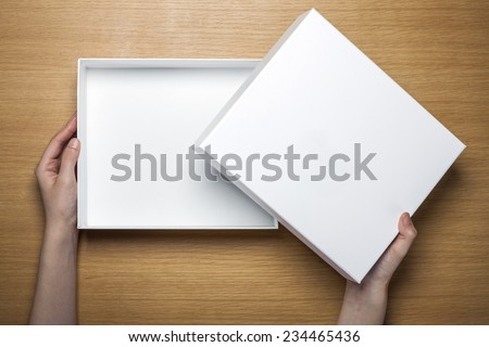 A female(woman) hands hold a empty(blank) white box on the desk(table) top view at the studio.