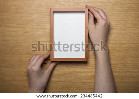 A female(woman) hands hold a wood photo(picture) empty(blank) frame on the desk(table) top view at the studio.