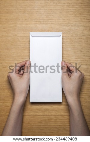 A female(woman) hands hold a white blank(empty) envelope on the desk(table), top view at the studio.