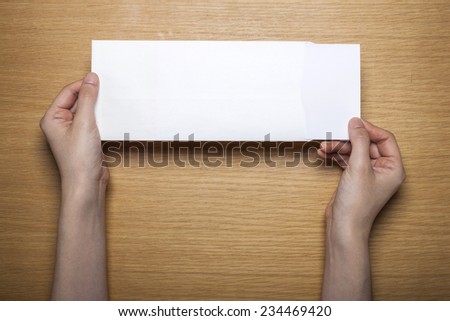 A female(woman) hands hold a white blank(empty) envelope on the desk(table), top view at the studio.