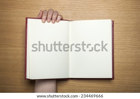 A female(woman) hands hold a blank(empty) book(note, diary) on the wood desk(table), top view at the studio.