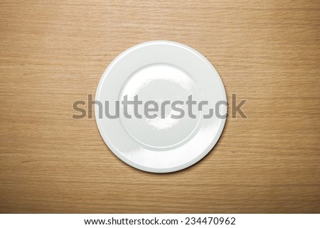 A female hands hold a empty(blank) white dish(plate) on the wood table(desk), top view at the studio.
