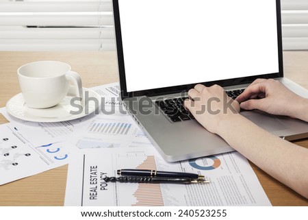 A working wooden desk(table) with notebook computer, coffee cup, paper, pencil, behind white blind(roller blind) and hand.