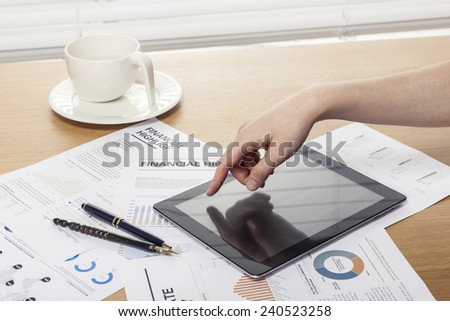 A working wooden desk(table) with tablet pc, coffee cup, graph, paper, pencil and hand behind white blind(roller blind, shade).