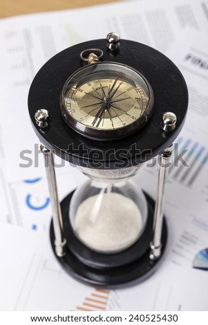 A wood working(office) table(desk) with sand timer(hour glass), graph paper(document)s for business, vintage compass, top view.