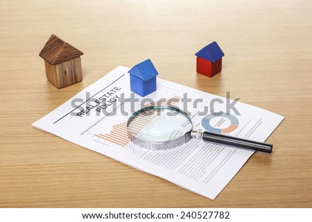 Three Houses made in wood block with a magnifier(reading glasses, magnifying glass[lens]) and graph paper(documents)s on the wood desk(office table).