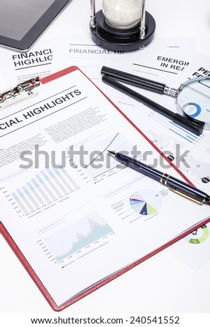 A red clipboard with graph documents and pen, tablet pc, sand timer at the studio,