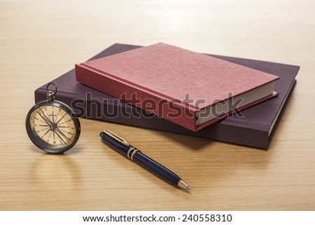 A vintage compass, pen, red book, diary, sketch book on the wooden office desk(table) .