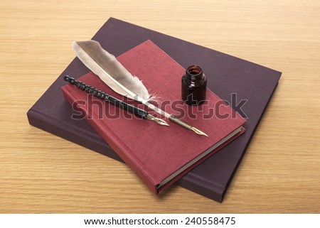 A ink, feather quill pen, red book, diary, sketch book on the wooden office desk(table) behind white blind.