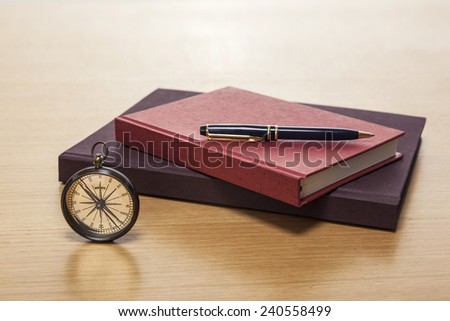 A vintage compass, pen, red book, diary, sketch book on the wooden office desk(table).
