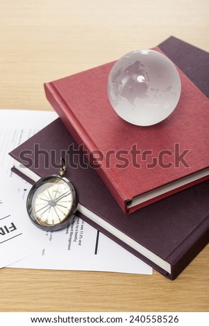 A magnifier, glasses, glass globe, compass, graph paper(document), clipboard and book on the wooden office desk(table).