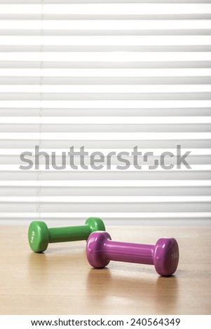 two dumbbells on the wood office desk(table) behind white blind.