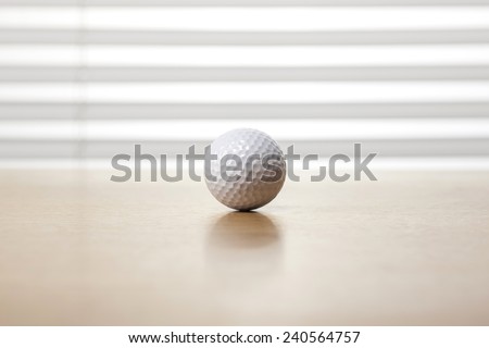 A golf ball on the wooden office desk(table) behind white blind.