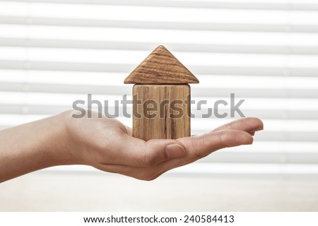 A female(woman) hand hold a house(made in wood blocks) white blind background and table.
