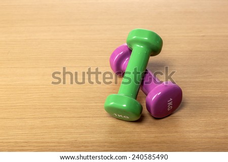 Two green and pink(magenta) dumbbells on the wood office desk(table).