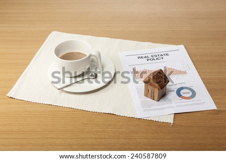 A coffee cup, wood house(wood block), graph paper(document) on the office desk(table).