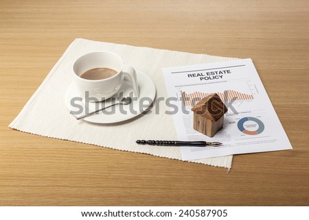A coffee cup, wood house(wood block), pen, graph paper(document) on the office desk(table).