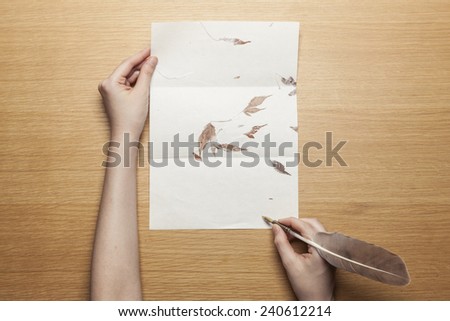 A female(woman) hand hold(write) a feather quill pen on the letter paper and wood desk(table) top view at the studio.