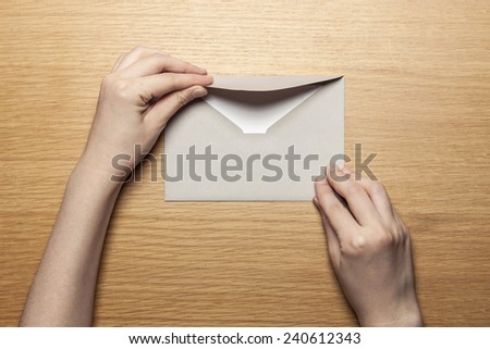 A female(woman) hand hold(open) a envelope and post card on the wood desk, top view at the studio.