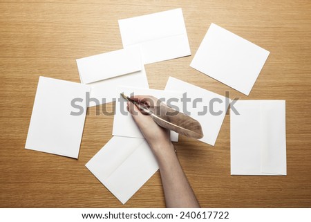 A female(woman) hand hold a feather quill pen with letter paper and envelopes on the wood office desk(table) top view at the studio.
