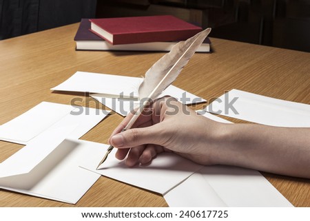A female(woman) hand hold a feather quill pen with letter paper and envelopes on the wood office desk(table) at the studio.