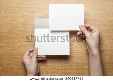 A female(woman) hand hold(open) a envelope and post card on the wood office desk(table) top view at the studio.