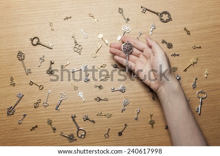 A female(woman) hand hold a vintage key among various keys on the wood office desk(table) top view at the studio.