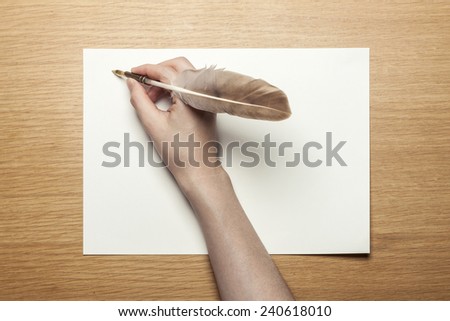 A female(woman) hand hold a feather quill pen with letter paper on the wood office desk(table) top view at the studio.