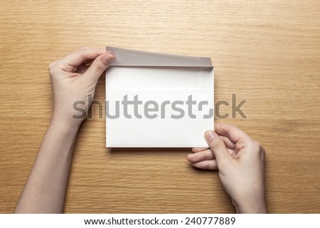 A female(woman) hand hold a envelope on the wood desk.
