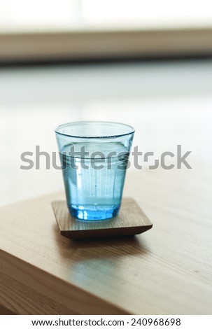 A blue glass cup of water on the table(desk), day light in the morning.