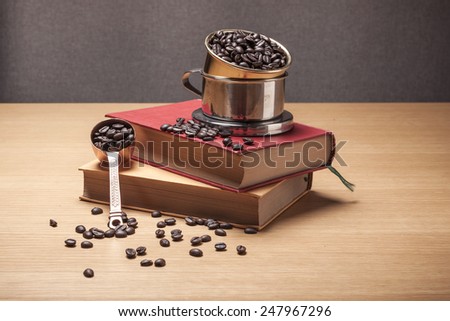 A coffee brass spoon with coffee beans and old(vintage, classic) book and coffee dripper on the wood table(desk).