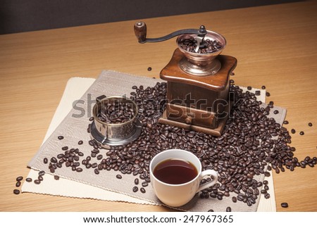 A brass coffee dripper, grinder, white cup, beans, table cloth on the wood table(desk).