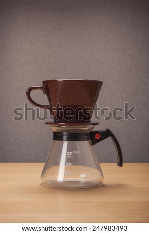 A brown ceramic coffee cup(dripper) and glass pot for hand drip coffee on the wood table(desk).