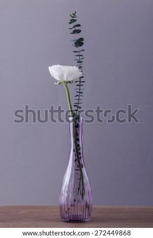 A white flower and leaves in the glass vase on the tale(desk) in the studio..