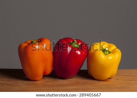 Three colorful fresh red, orange, yellow sweet pepper(pimenta, bell pepper, pimento) on the wood table(desk) in the grey background at the studio.