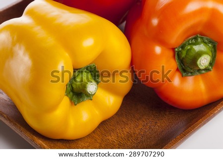 Three colorful fresh red, orange, yellow sweet pepper(pimenta, bell pepper, pimento) close up on the wood dish(tray, bowl) isolated white at the studio.
