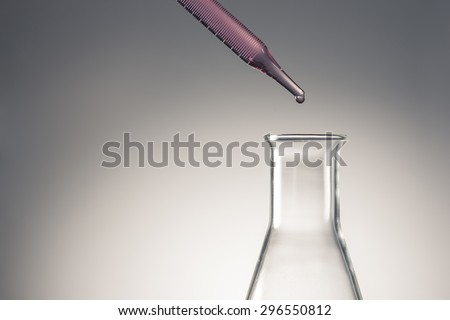 A man\'s hand hold and lean a glass dropping pipet(dropping pipette, medicine dropper, spuit) with red(magenta, pink) water(liquid, fluid) to the glass Erlenmeyer flask in the laboratory
