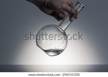 A man\'s hand hold and lean, shake a glass flat bottom flask with water(liquid, fluid) on the desk in the laboratory