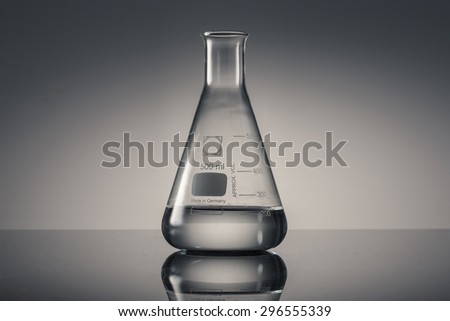 A glass Erlenmeyer flask with water(liquid, fluid) on the reflected black desk in the laboratory