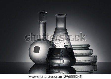 A flat bottom flask, a erlenmeyer flask, petri dish(Schale) on the reflected black desk in the laboratory