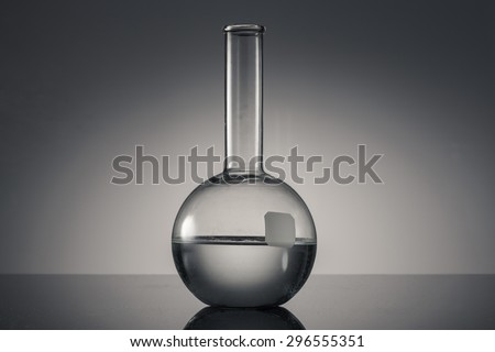 A glass flat bottom flask with water(liquid, fluid) on the reflected black desk in the laboratory