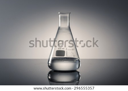 A glass Erlenmeyer flask with water(liquid, fluid) on the reflected black desk in the laboratory
