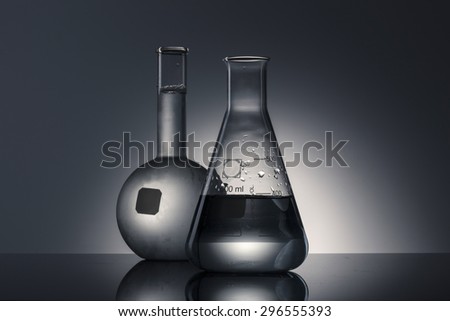 A flat bottom flask, a erlenmeyer flask on the reflected black desk in the laboratory