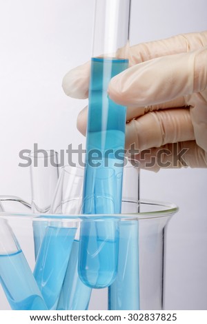 A woman(nurse, scientist) hand with (rubber) glove storage hold a test tube with blue(cyan) liquid(fluid) and beaker for chemical, health at the laboratory