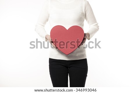 A woman(girl, female) wearing white sweater(shirts), black pants hand hold a red heart(love) gift box(package) isolated white at the studio.