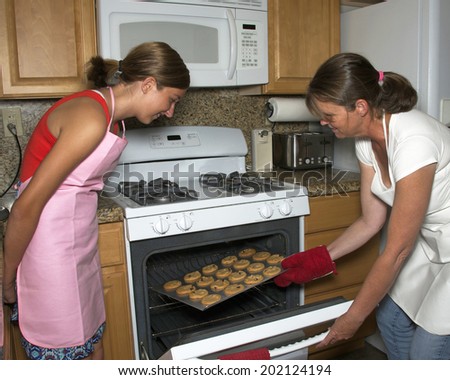 Mother and daughter baking cookies together, taking cookies out of the oven